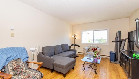 A living room with a grey couch, a chair with a floral pattern, a coffee table, and a television.